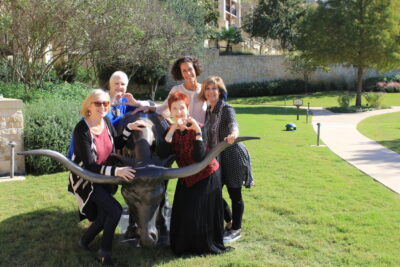 Five women posing with longhorn statue outdoors.